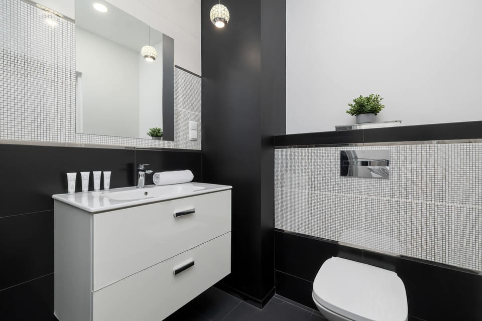 A modern bathroom vanity features a large rectangular sink and a wide mirror that reflects the room. The textured black and white tiles on the wall add a bold architectural detail.