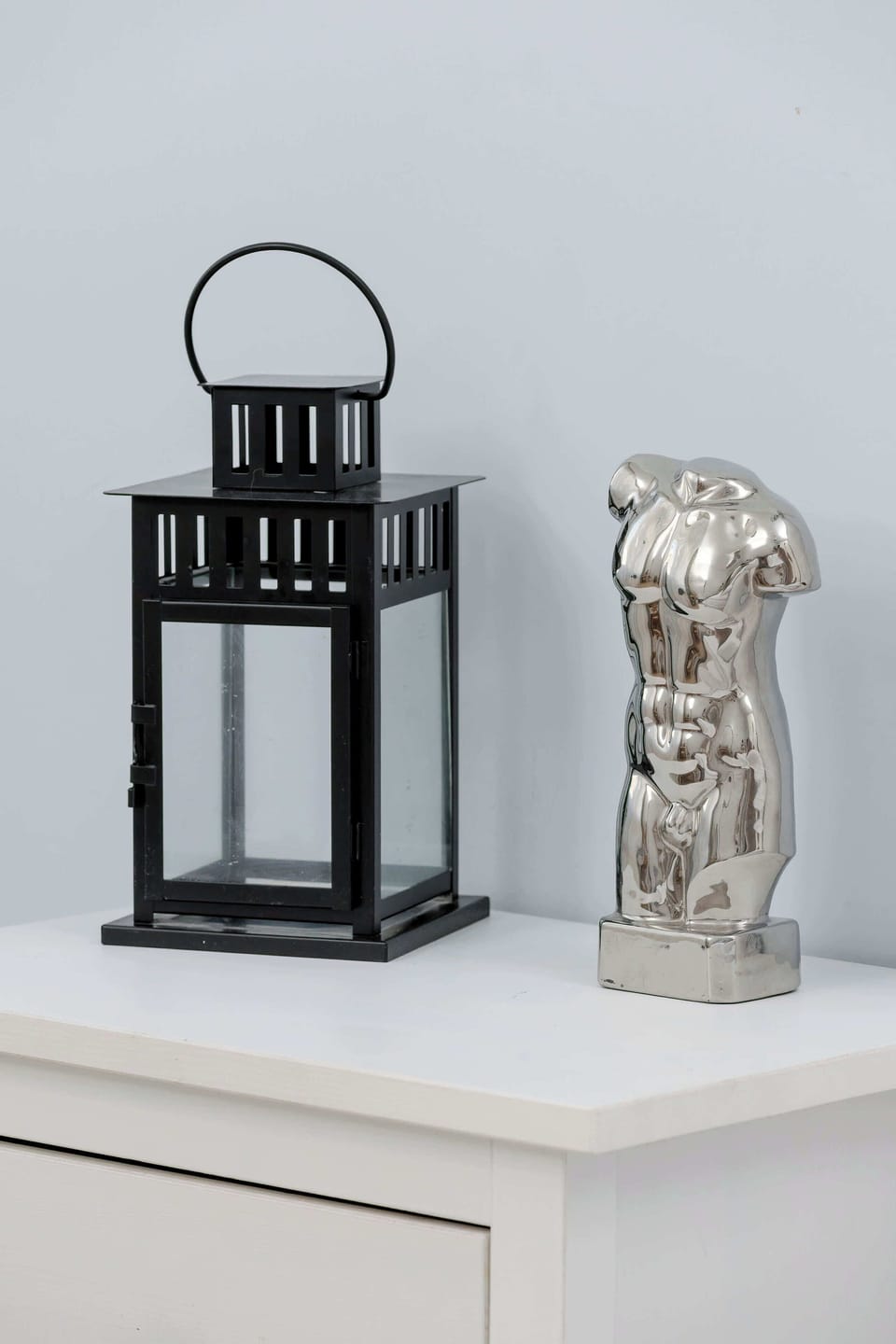 A black metal lantern and a silver Buddha figurine are neatly arranged on top of a white chest of drawers. These decorative elements add a peaceful and personal touch to the interior.