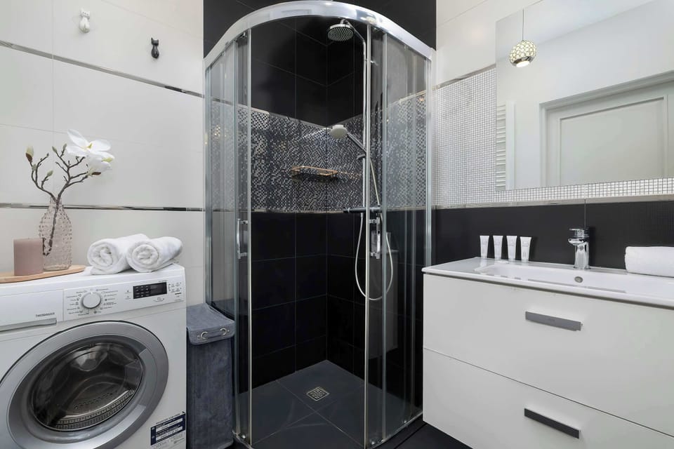 A contemporary bathroom design featuring a glass shower cabin, white vanity, and large mirror.  The black and white tile accents add a touch of sophistication.