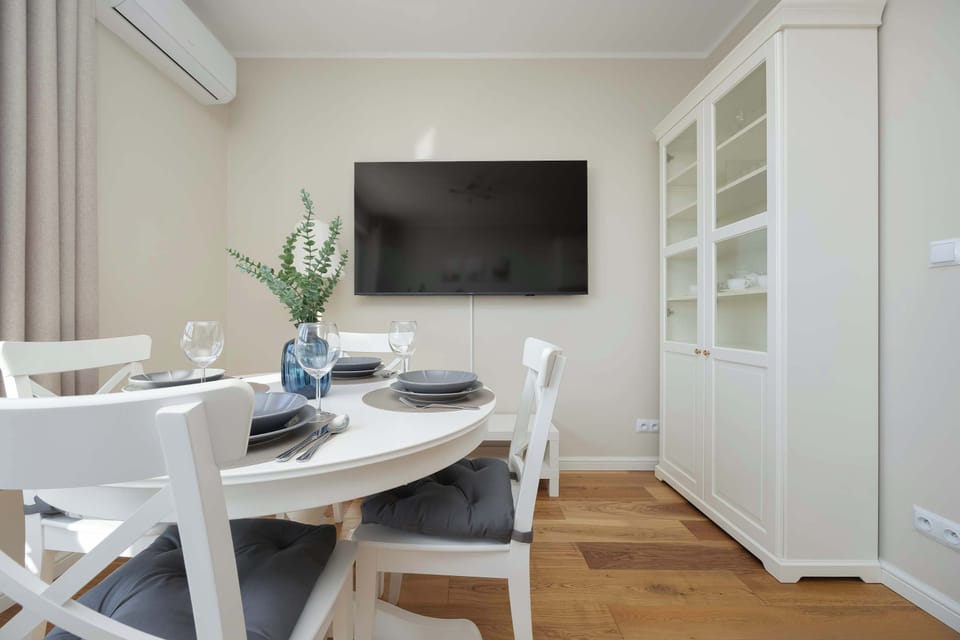 A dining space with a round white table set with plates and glasses, next to a TV and a glass-front cabinet.