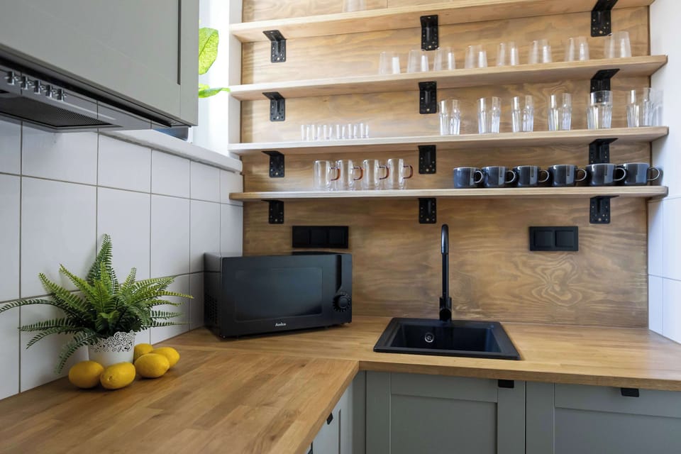 The view of the kitchen countertop showcases a modern black sink and faucet, as well as spice jars arranged on open shelves. In the corner is a small microwave, perfect for quickly heating up food.