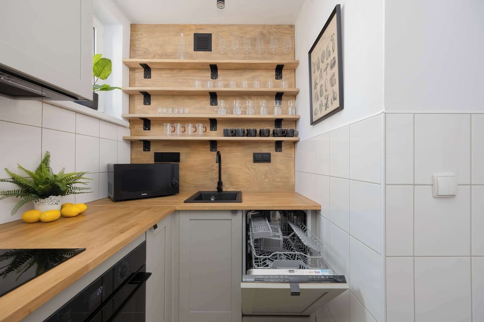 The kitchen is equipped with a modern built-in dishwasher, which makes it much easier to keep things tidy during a longer stay. Open shelves above the countertop display neatly arranged glasses and mugs, ready for guests to use.