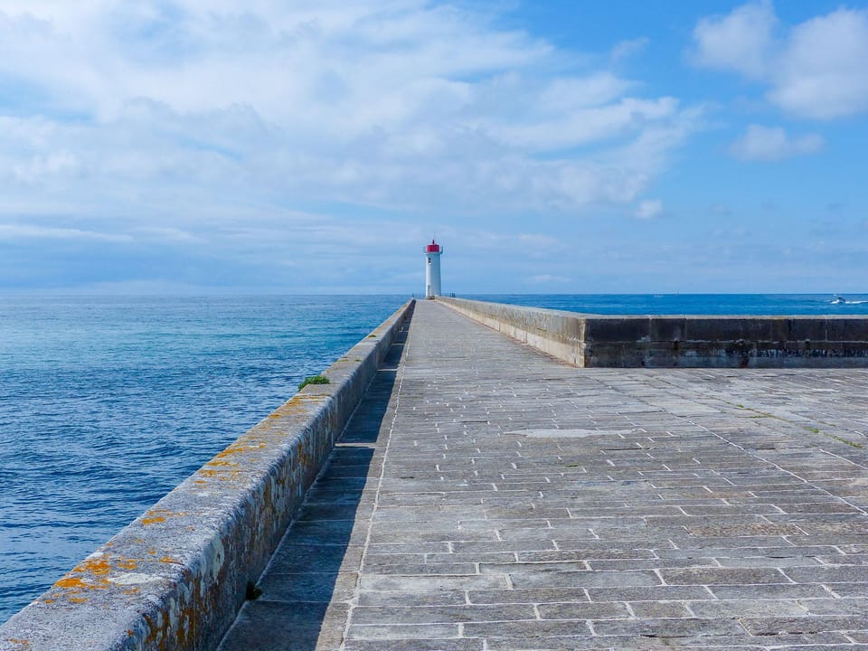 Stroll along the pier, enjoying expansive views of the tranquil sea and distant lighthouse.