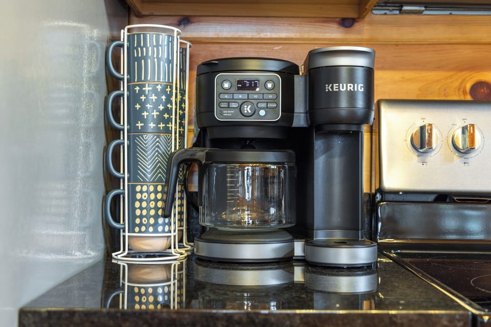 A dual coffee maker and stacked mugs sit ready for the first pour of the morning.