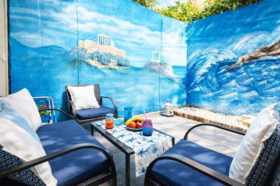 Charming outdoor seating area featuring a vibrant mural inspired by the Aegean Sea and Cape Sounio. Comfortable loungers and a relaxed setting create a unique space to enjoy morning coffee, read a book, or unwind outdoors 
