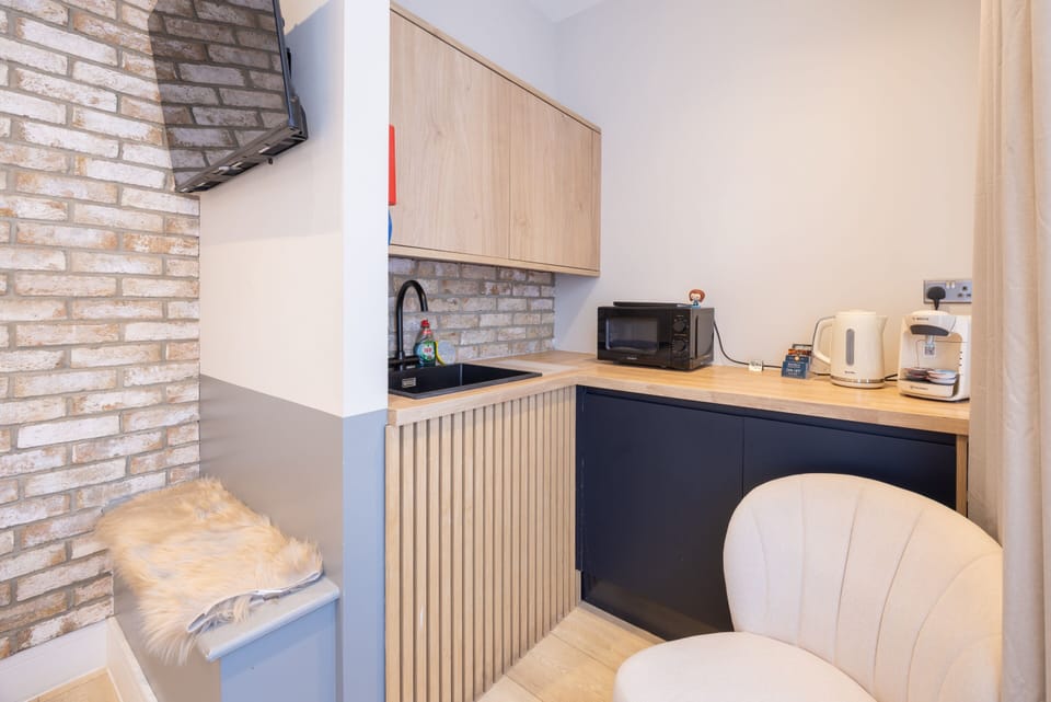Experience a stylish modern studio with chic decor, a cosy lounge chair, smart TV, tea and coffee making facilities, and a microwave for your convenience.