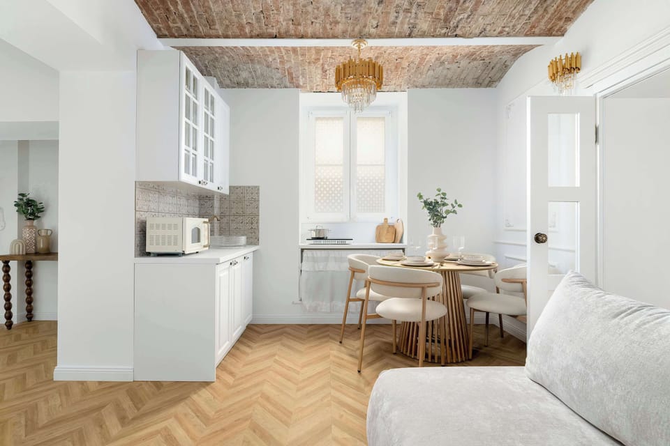 This angle captures the transition between the kitchen and dining zones, showing the white cabinetry and microwave. The layout is compact yet functional, defined by the consistent use of light wood and white finishes.