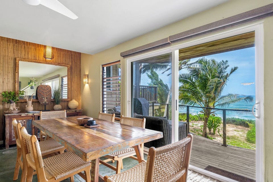 The tropical dining room frames stunning ocean views through floor-to-ceiling windows, where palm trees sway just beyond your private terrace.