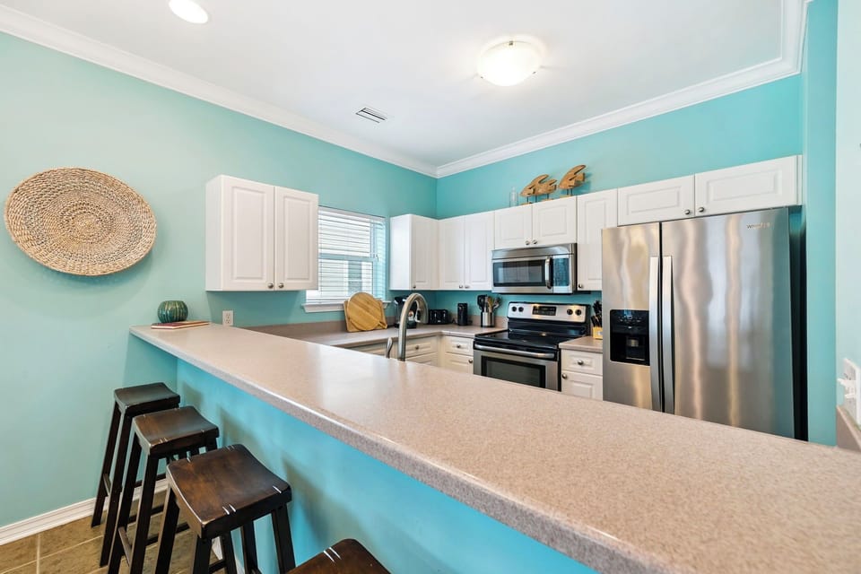 Your fully equipped kitchen features stainless steel appliances, generous counter space, and cheerful turquoise walls that create a bright, welcoming atmosphere for cooking.