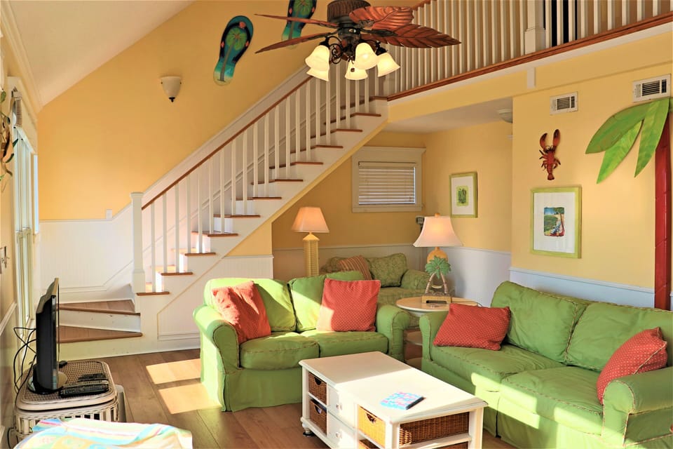 Relax in your vibrant tropical-themed living room with cheerful green sofas and colorful island décor creating the perfect beachy retreat atmosphere.