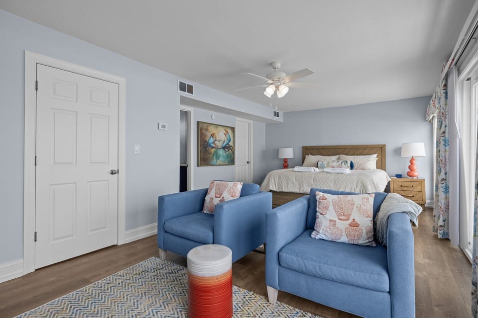 Relax in your spacious suite with cozy blue seating, comfortable bed, and calming coastal decor that creates the perfect retreat.