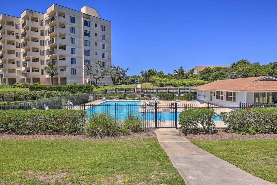 Modern residential complex featuring a pristine swimming pool surrounded by lush landscaping and mature trees under clear blue skies.