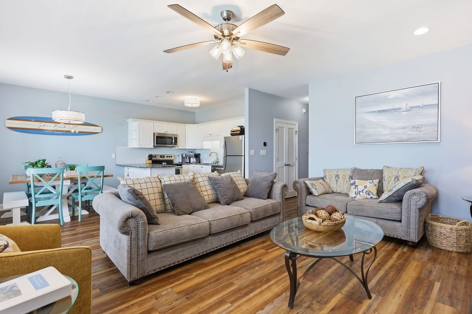 Relax in your spacious open-concept living area with coastal charm, comfy seating, ceiling fans, and a fully equipped kitchen ready for your stay.