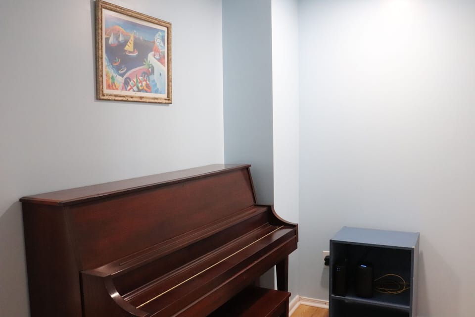 Your private music corner awaits, featuring a classic upright piano ready for impromptu melodies and a cozy mini-fridge stocked for your refreshment, all set beneath cheerful artwork.
