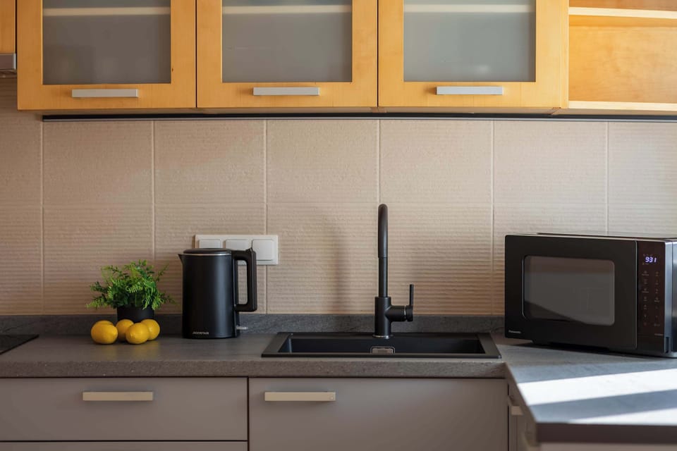 A detail of the kitchen countertop featuring a black sink, a modern faucet and an electric kettle.