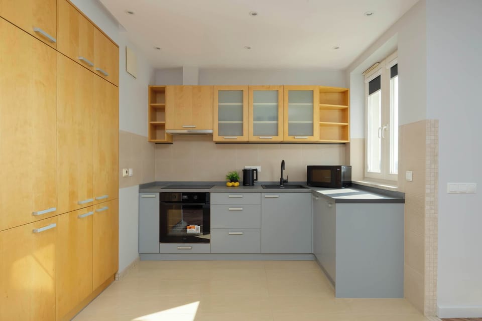 A functional L-shaped kitchenette, equipped with light gray cabinets, a black countertop, and a modern oven and stovetop.