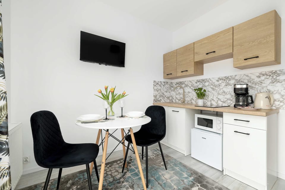 A functional kitchenette with light wood cabinets and a compact worktop. A small dining setup is placed right beside it, making efficient use of the limited space.