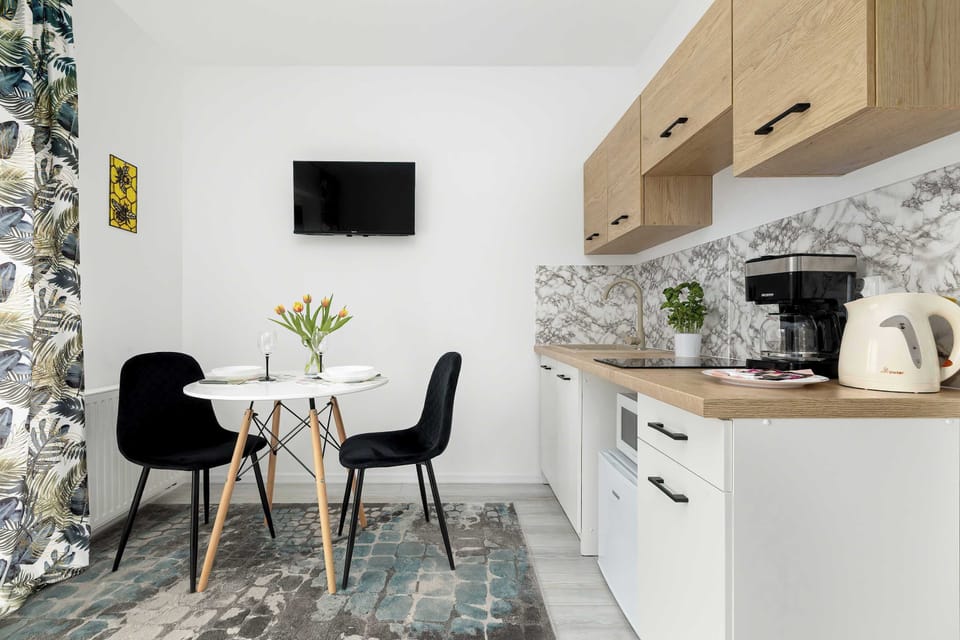 A dining corner next to a kitchenette, with a round table and two modern chairs. The backsplash has a decorative pattern, adding character to the clean, white cabinetry.