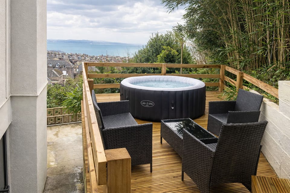 Spacious patio area with outdoor dining furniture and a private hot tub, ideal for relaxing evenings after a day exploring the Cornish coast.