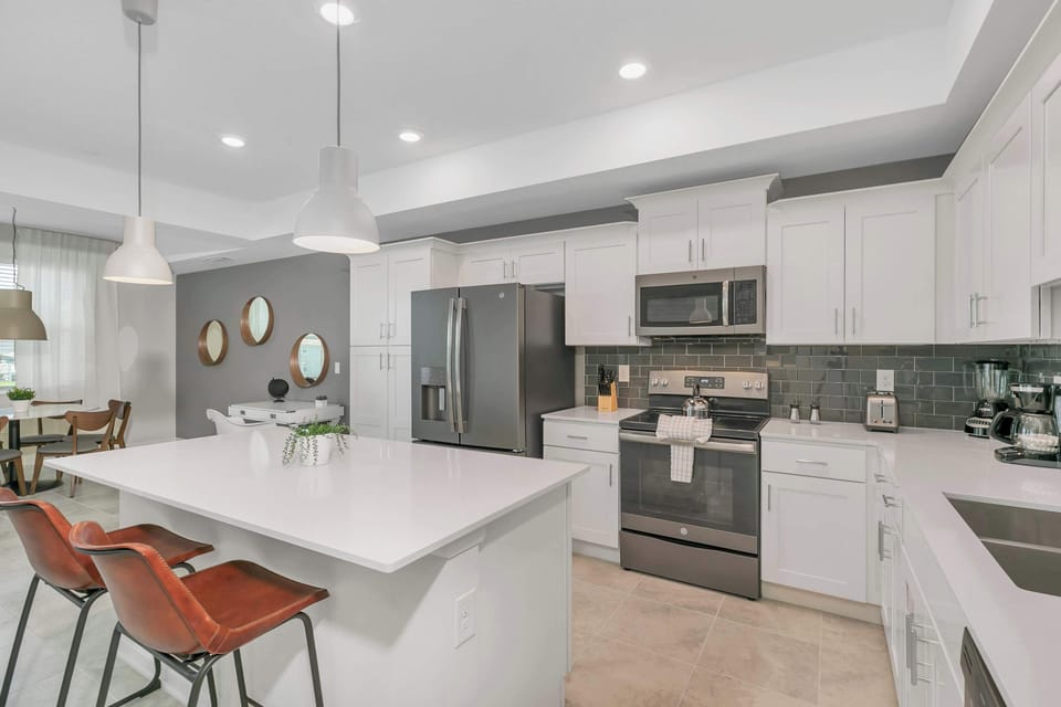 Whip up gourmet meals in this sleek, white kitchen featuring premium stainless steel appliances and a spacious breakfast bar.