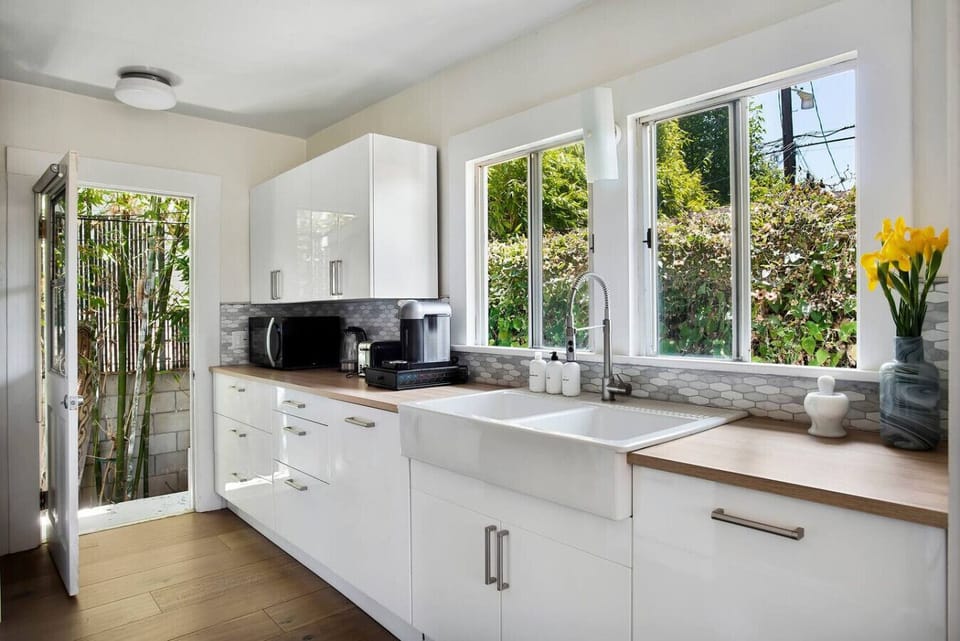 Cook like a local in this bright, fully equipped kitchen featuring a farmhouse sink, sleek white cabinetry, and a beautiful garden view through oversized windows.