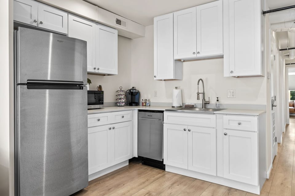 White kitchen with stainless refrigerator and dishwasher, deep sink, microwave, and single-serve coffee station.