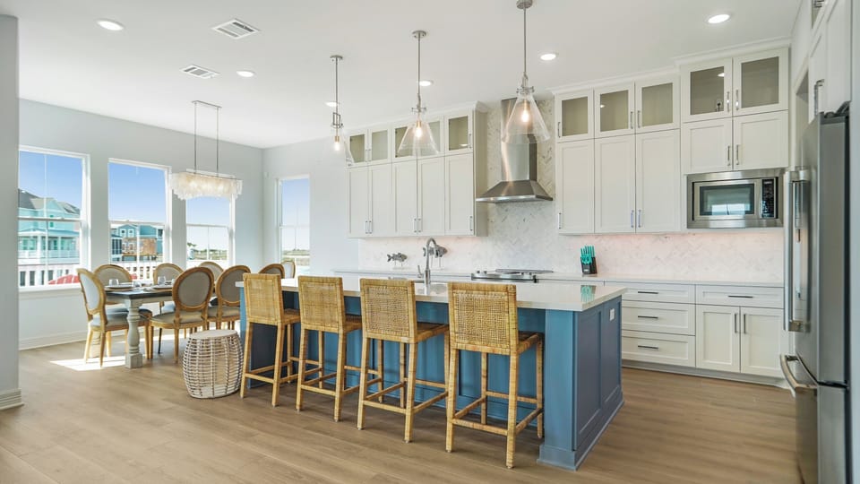 Large gourmet kitchen with island seating, stainless appliances, and modern lighting—perfect for cooking meals during your Galveston beach getaway.
