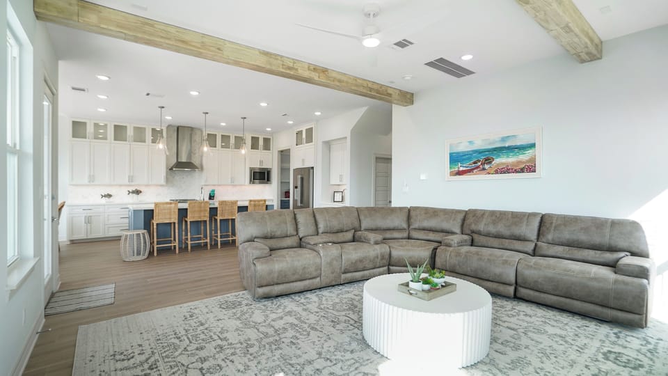 Bright open-concept living room with large sectional sofa, coastal decor, and direct connection to the kitchen and dining area—perfect for family gatherings.
