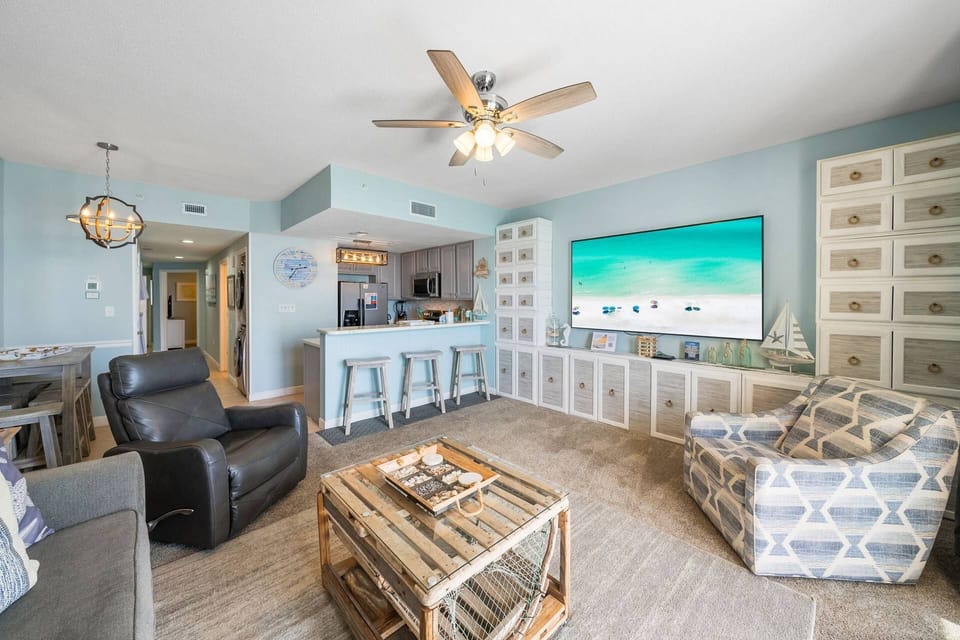 Coastal-chic living room with comfortable seating, a large-screen TV, bar seating, and charming nautical décor throughout.