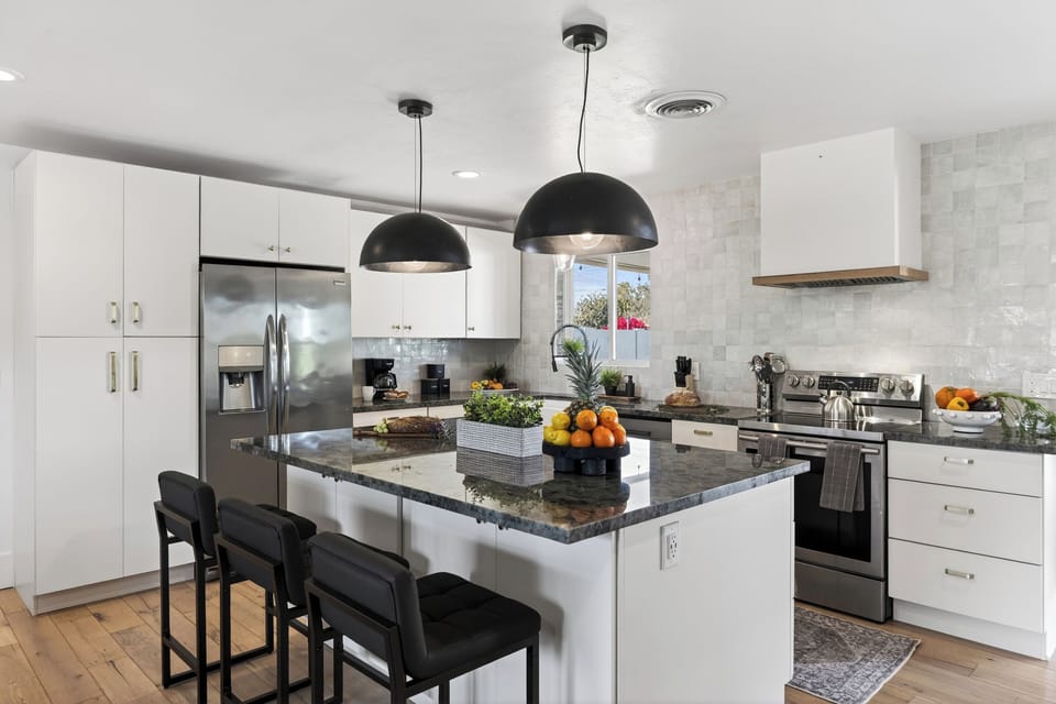 Modern kitchen with a large granite island and industrial pendant lighting.