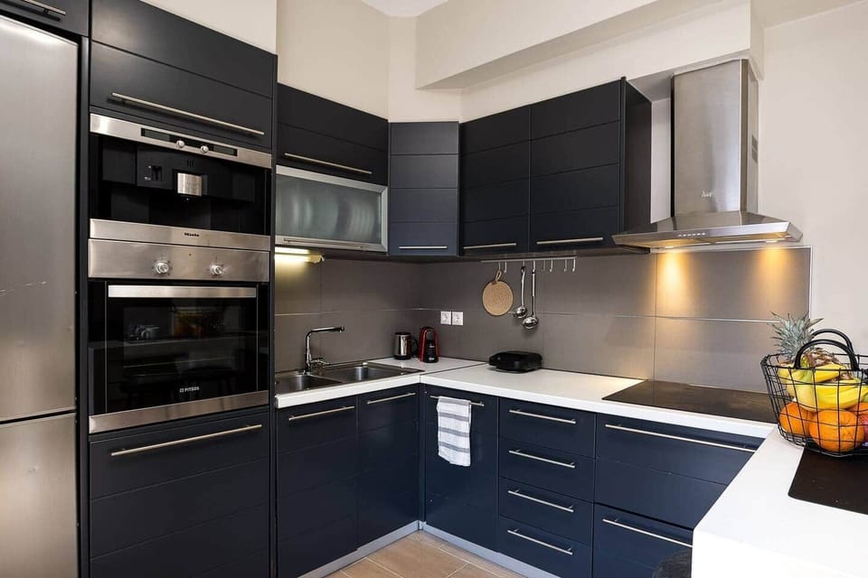 Stylish kitchen with dark cabinetry, generous counter space, and built-in appliances including an oven, cooktop, and full-size fridge. The practical L-shaped layout keeps everything within easy reach for relaxed everyday cooking.