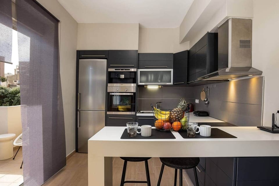 Modern kitchen with sleek cabinetry, a full-size fridge, built-in oven, and a breakfast bar with seating for two. The balcony door brings in natural light, while the efficient layout keeps cooking, dining, and morning coffee easy.