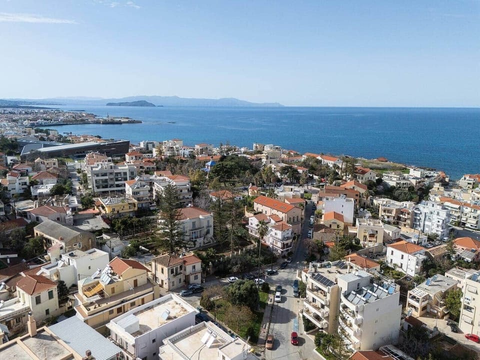 Residential neighborhood with low-rise buildings, nearby streets, and the sea visible in the distance. The area feels open and well connected, with the apartment set among local homes and close to the waterfront for an easy local stay.