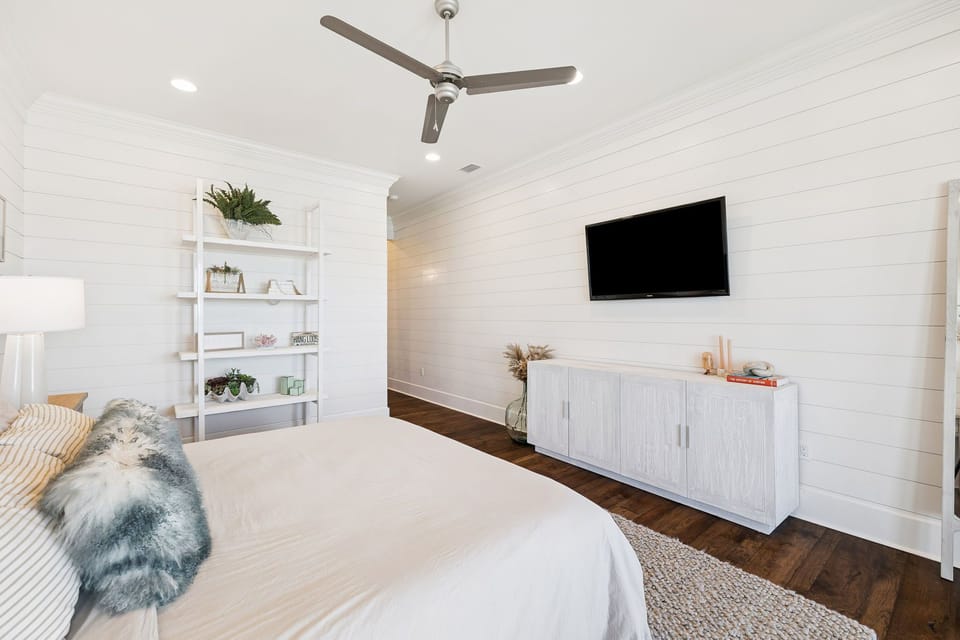 Drift off in this serene bedroom where crisp white linens meet cozy textures, your entertainment center ready for lazy mornings.
