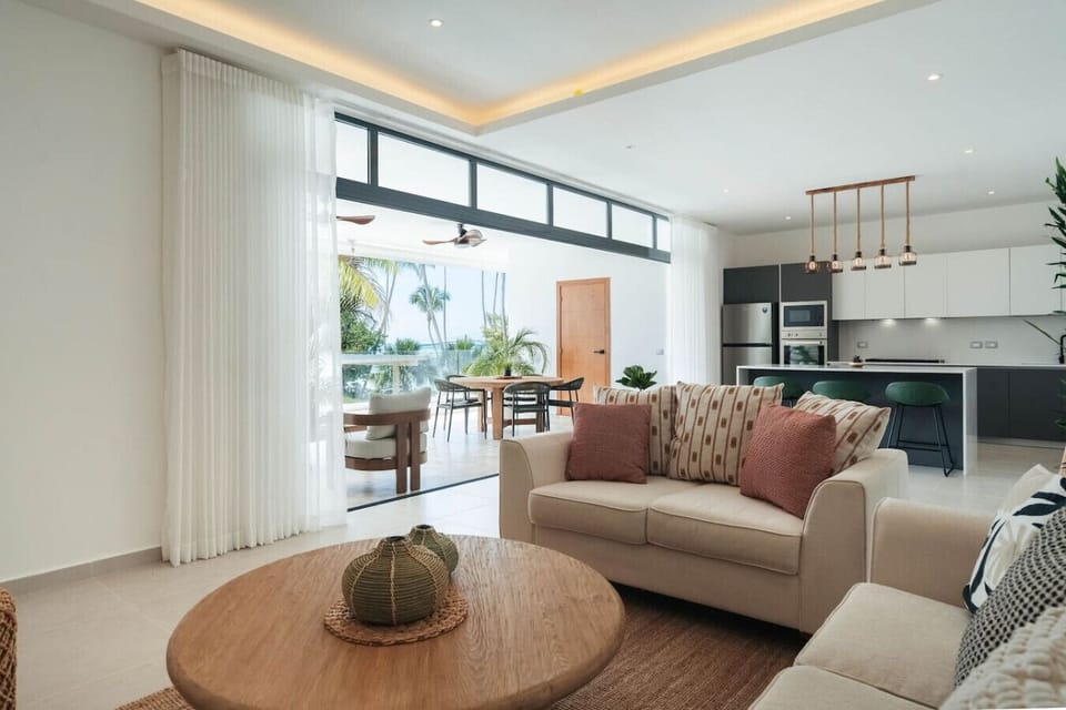 Open living space that flows straight out to the balcony—lots of natural light, comfy seating, and a partial ocean view. Easy spot to relax, dine, or just hang out with the breeze coming in.
