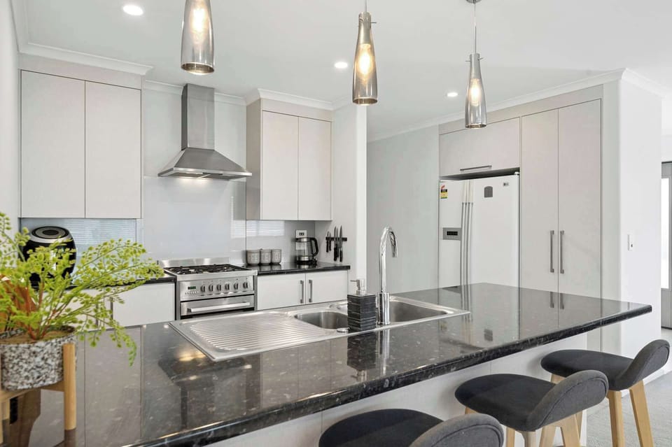 Granite island bench with double sink, gas range, rangehood and large fridge-freezer — fully equipped kitchen for self-catering in Rotorua