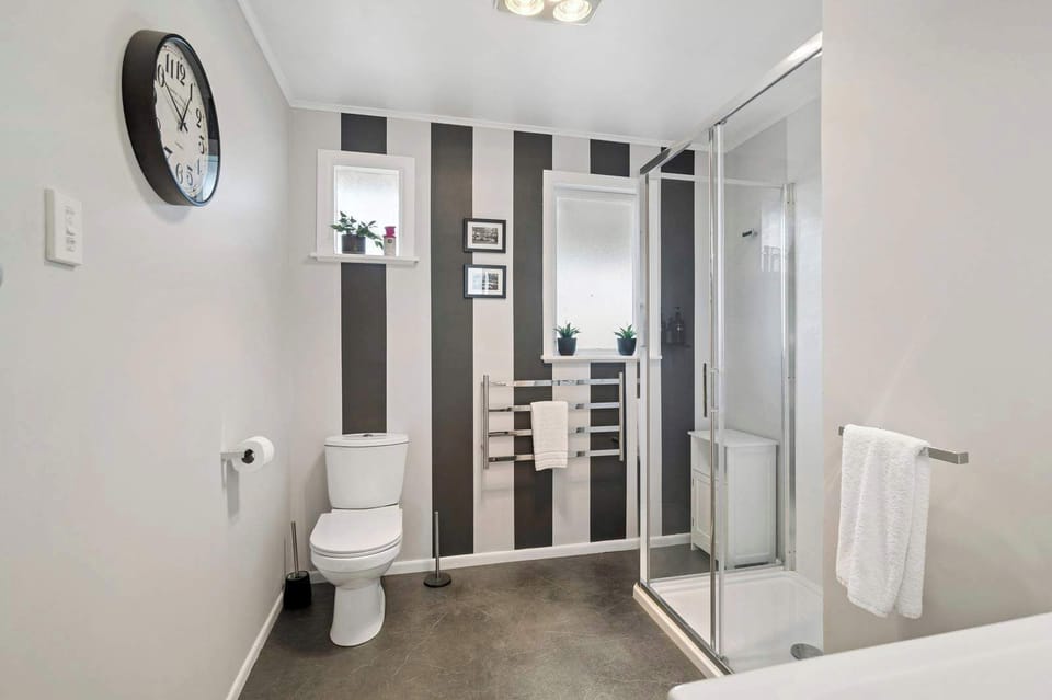 Full bathroom with toilet, walk-in shower, heated towel rail, and bold black-and-white feature wall — well-appointed NZ holiday rental Rotorua