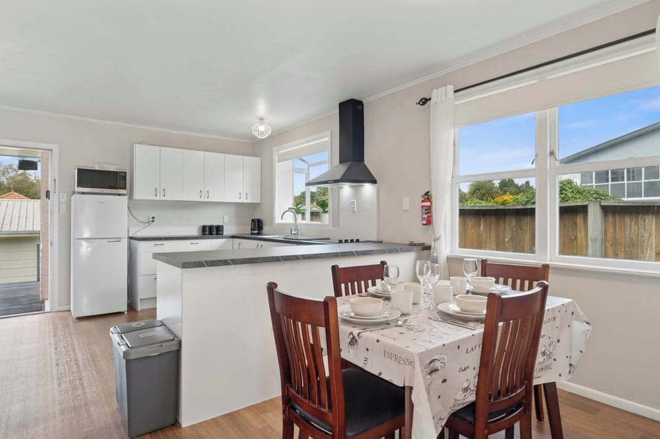 Open-plan kitchen and dining area with 4-seat table, white cabinetry, and large sun-filled windows — Rotorua self-contained holiday home