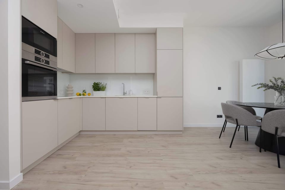 A sleek and modern kitchen with white cabinets and built-in appliances. The minimal design enhances the open-plan layout.
