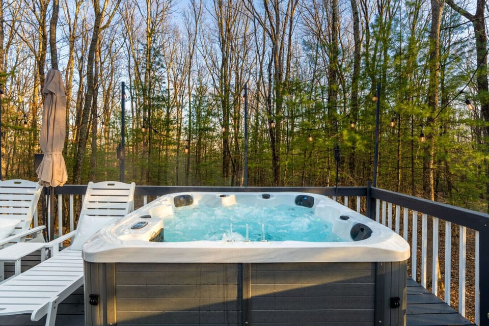 Relaxing in hot tub on the deck surrounded by string lights and forest views. A perfect spot to unwind and soak after a day of exploring the Poconos.