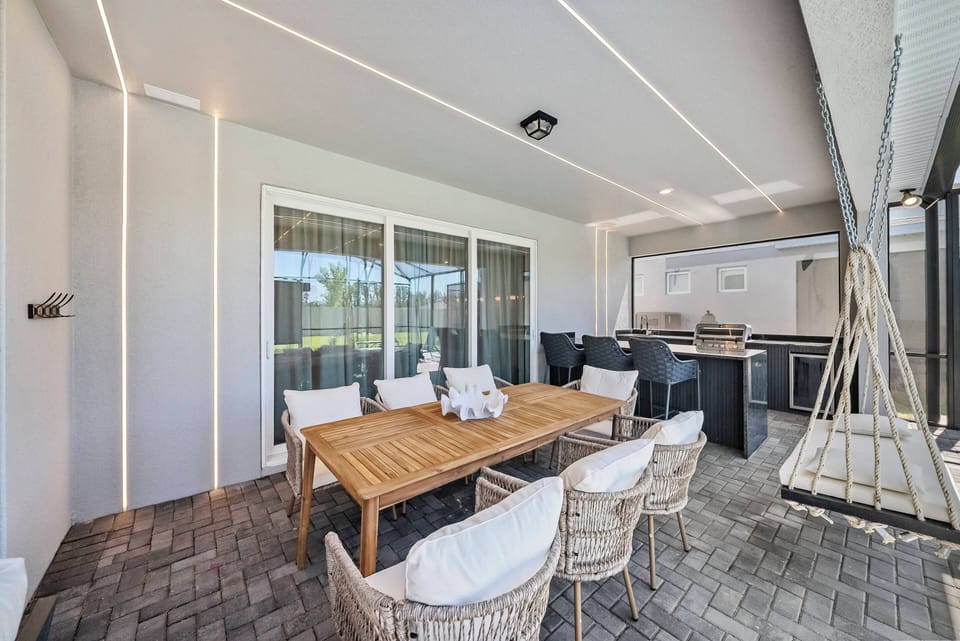 Step outside to enjoy a spacious dining area with a lovely wooden table and comfy woven chairs. Large sliding glass doors let in natural light and create a perfect flow between indoor and outdoor living for your gatherings.