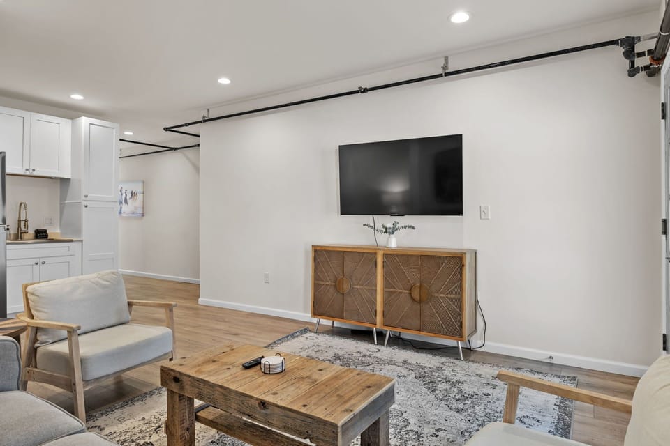 Wall-mounted TV and wooden media console face the living-room seating.