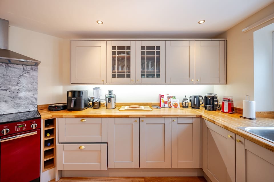 Prepare meals in a bright, well-equipped kitchen featuring a red oven, wine racks, and modern appliances, all framed by warm wood and elegant cabinetry.