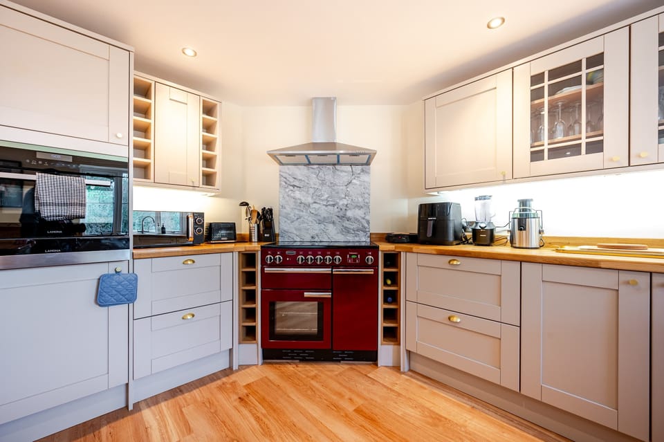 Cook in style with a striking red oven, marble backsplash, and U-shaped layout. Brass accents, wine racks, and warm wood tones create a kitchen that’s both modern and inviting.