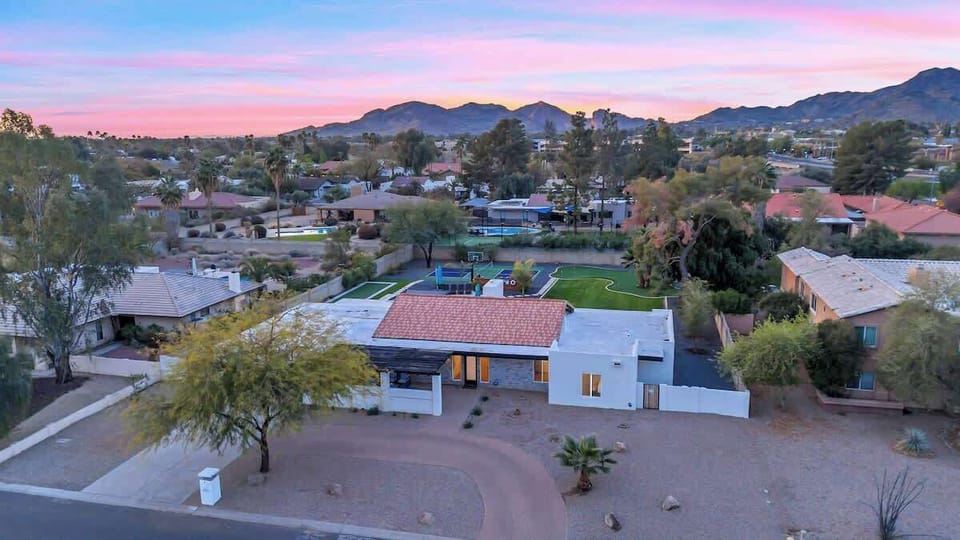Modern desert home nestled in scenic mountain foothills with vibrant sunset skies painting the neighborhood in warm hues.