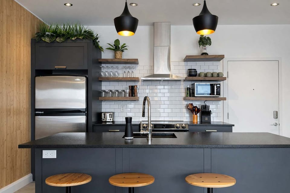 Cuisinez avec style dans cette cuisine moderne et entièrement équipée. Avec ses luminaires industriels, ses étagères en bois et son grand îlot central, c'est l'endroit idéal pour un café matinal ou un bon repas fait maison.