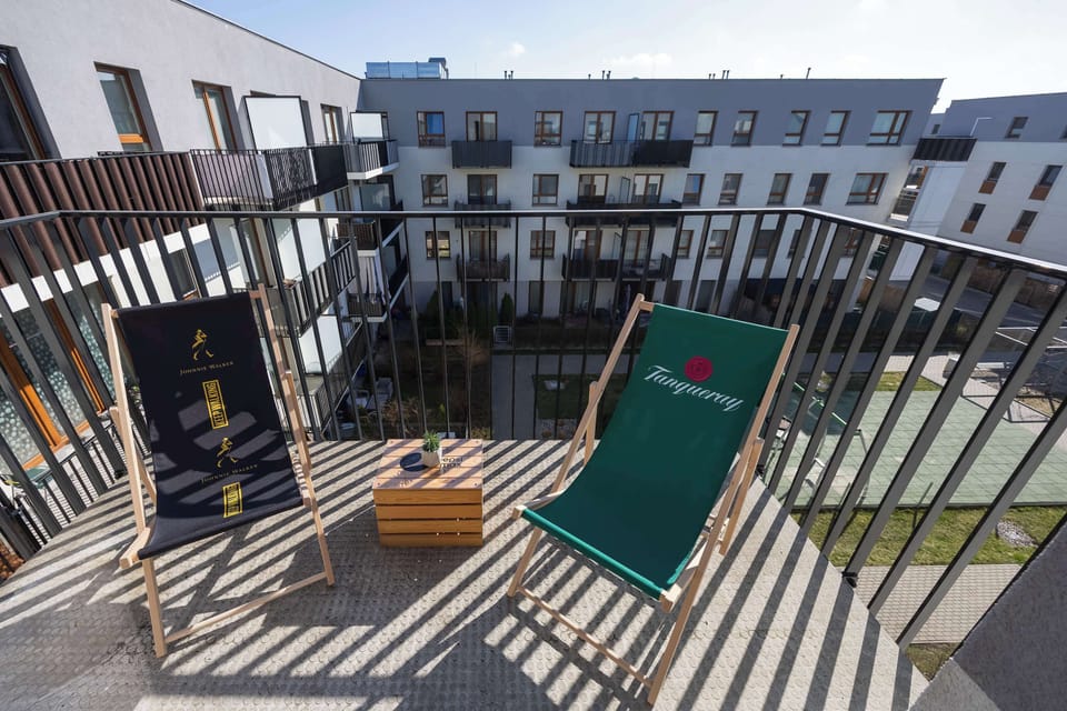 Private balcony is outfitted with two green lounge chairs and a small wooden crate used as a table. Striped shadows from the railing create a rhythmic pattern across the deck.