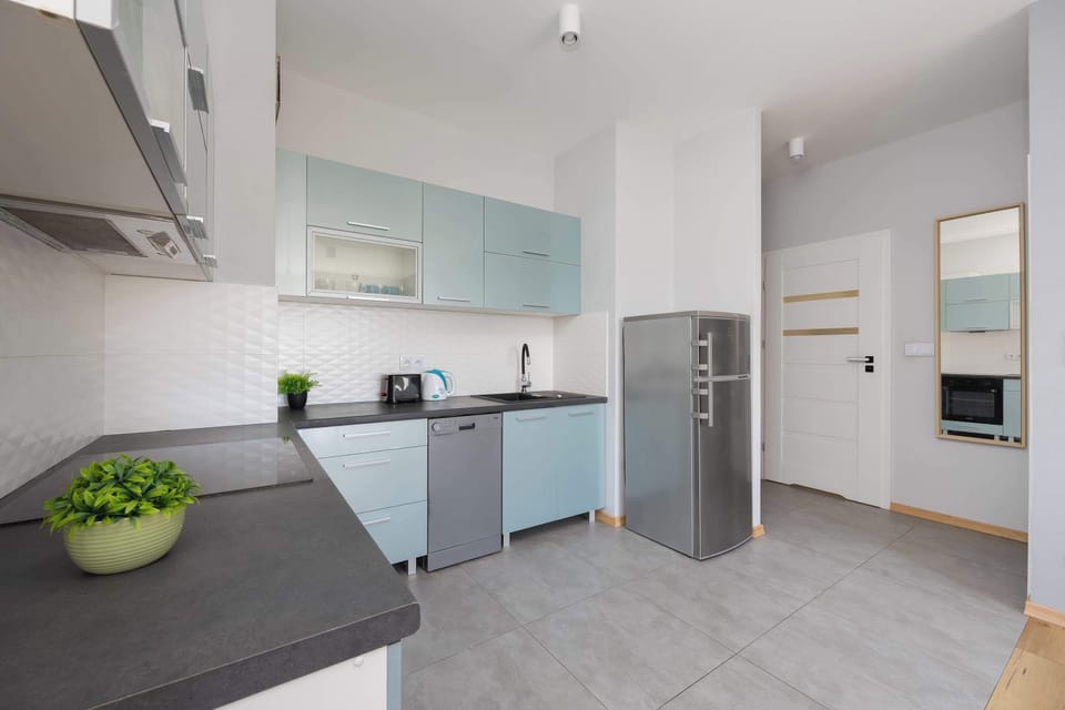 Modern kitchen showcases light teal cabinetry paired with a grey countertop and a stainless steel refrigerator. The layout is functional and open, blending seamlessly into the rest of the apartment.