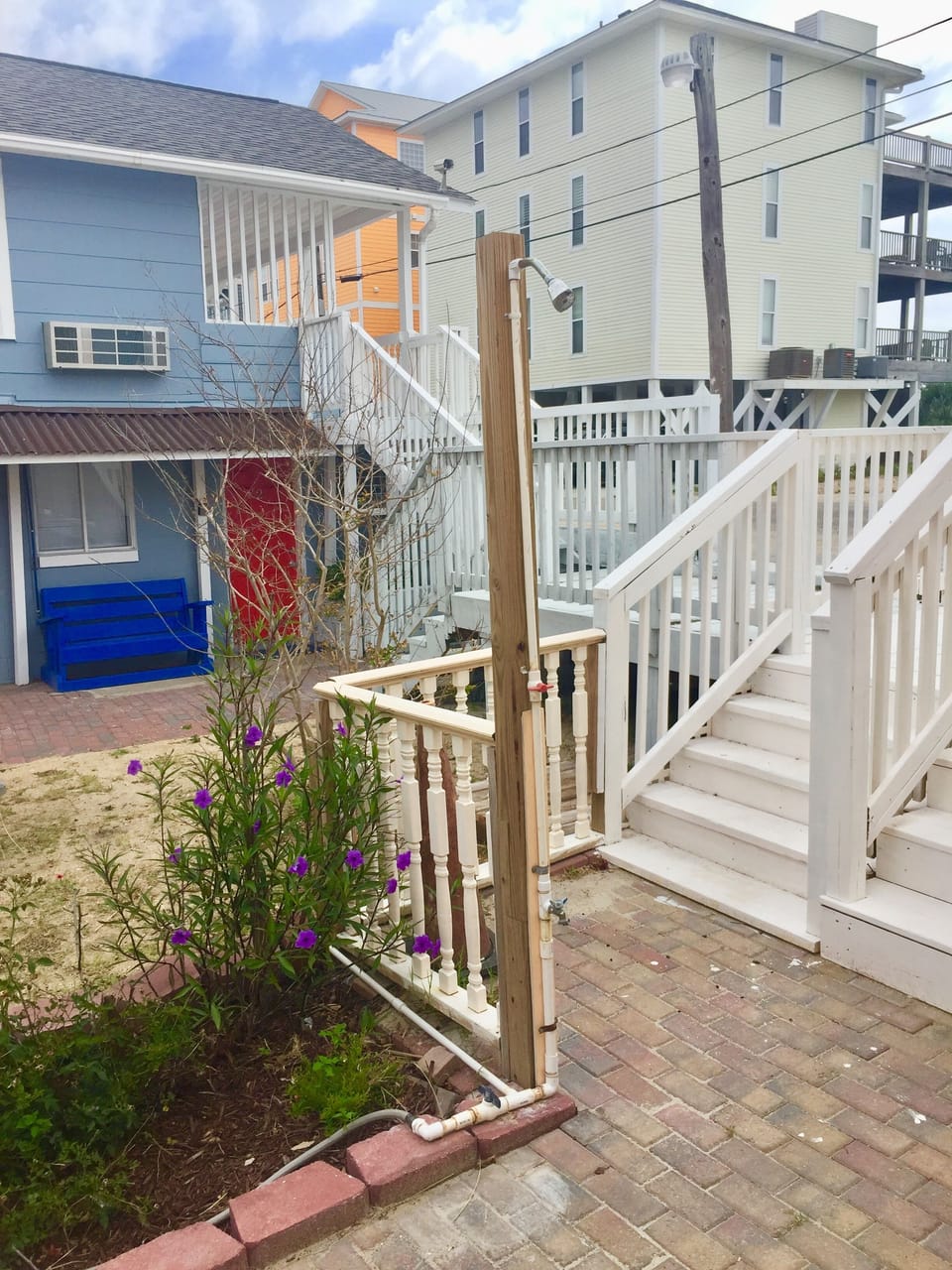 Colorful beachside property featuring elevated design with staircases and outdoor shower area surrounded by coastal landscaping.