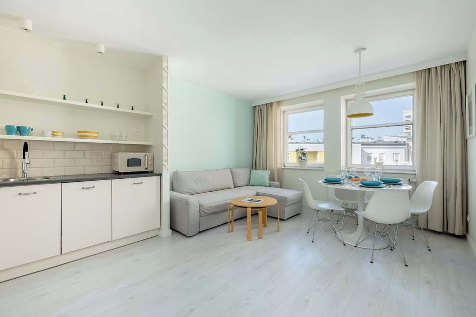 A spacious open-plan area combining a kitchenette and dining space. Light-colored cabinets and a small dining table near the window give the room a clean, modern feel.